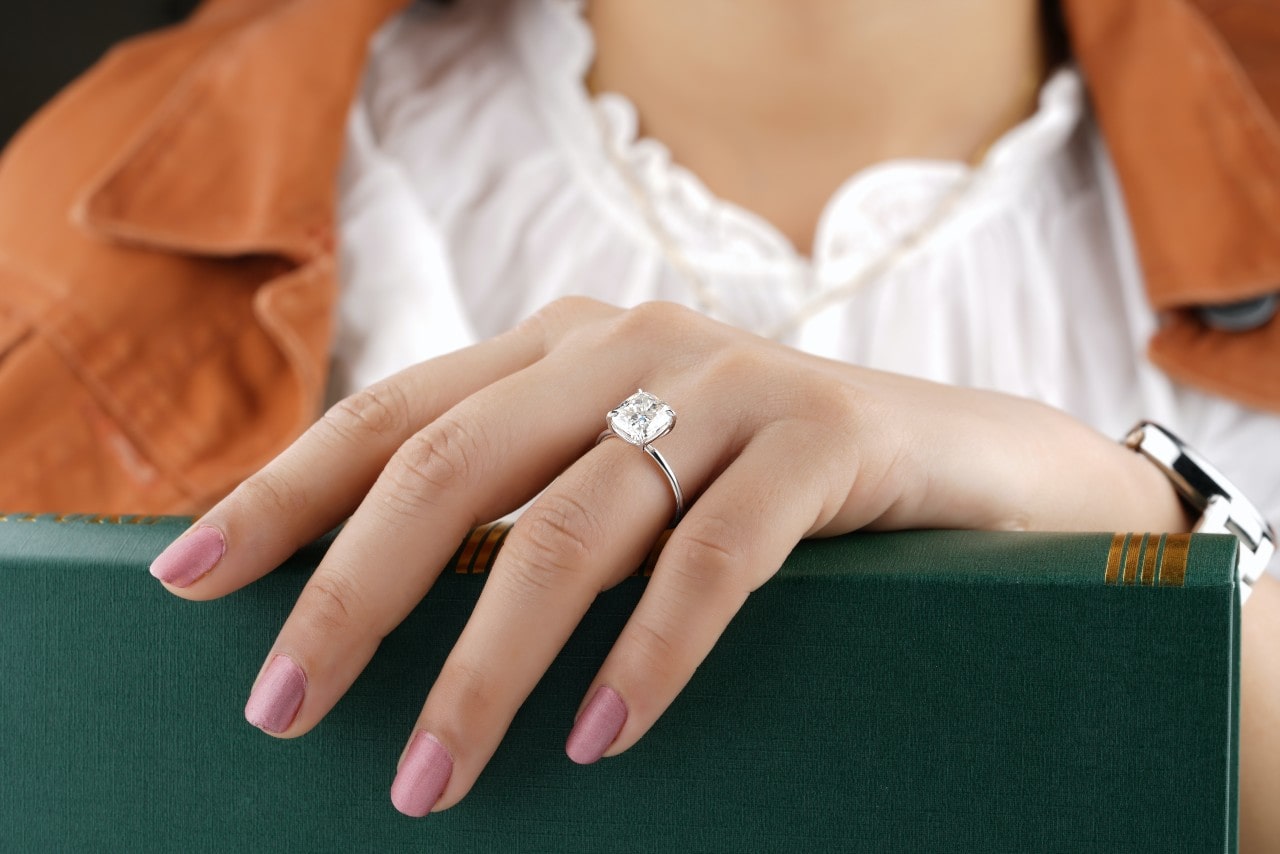 lady’s hand wearing a classic engagement ring holding a green book