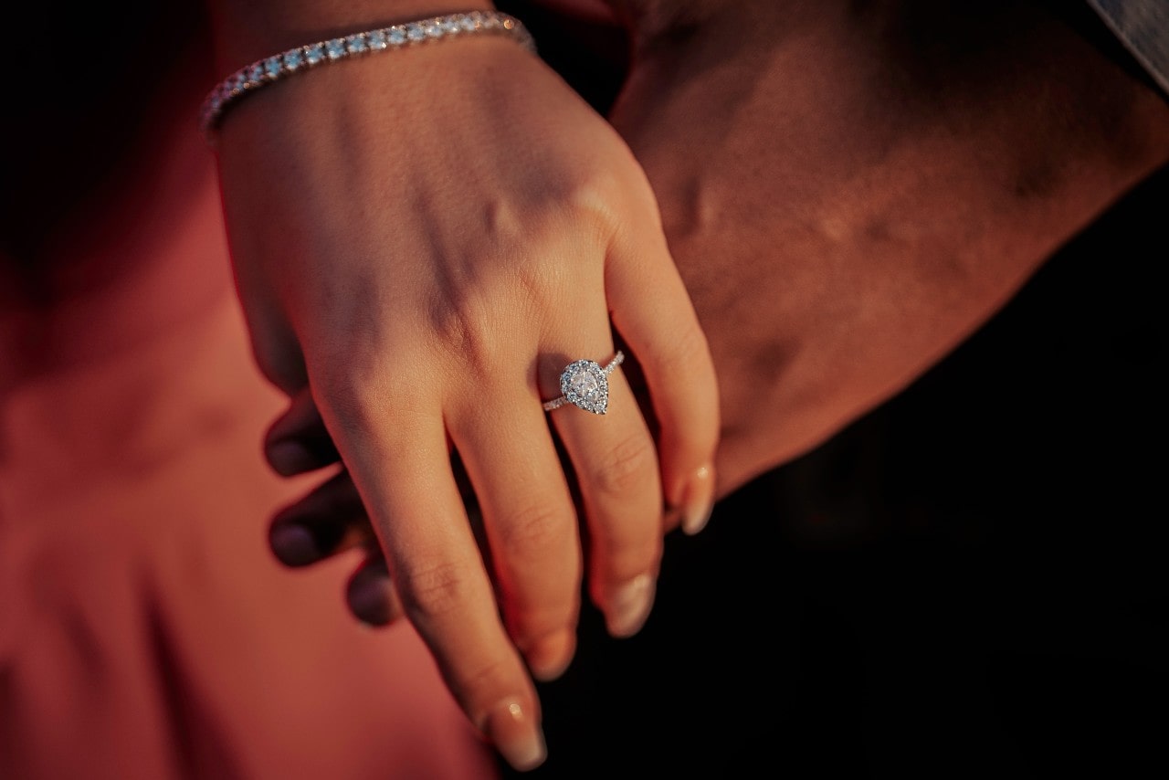 a lady’s hand wearing an engagement ring and holding a man’s hand