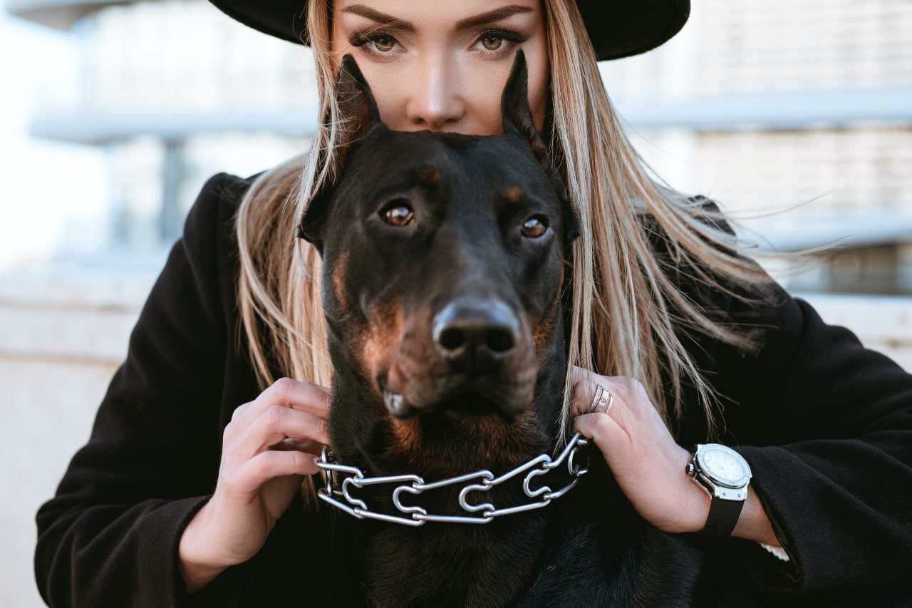 a woman holding the collar of her doberman and wearing a diamond studded watch