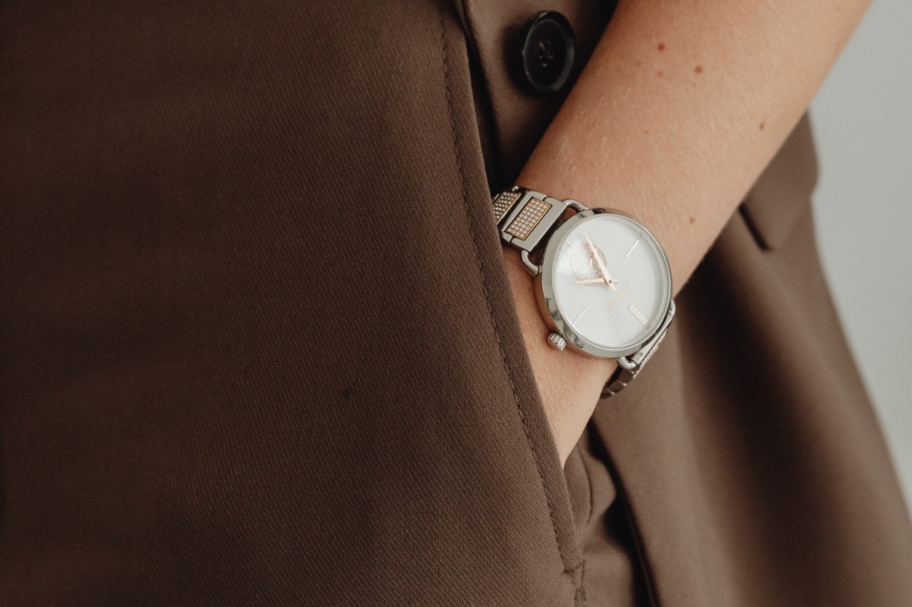 a woman’s hand in her trouser pocket, wearing a mixed metal watch with a diamond accented strap