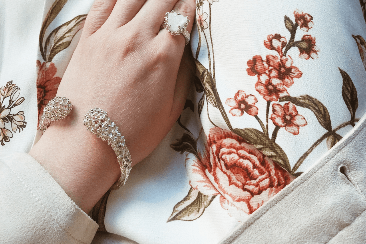 a closeup of a hand wearing white gold jewelry, touching a floral blouse.
