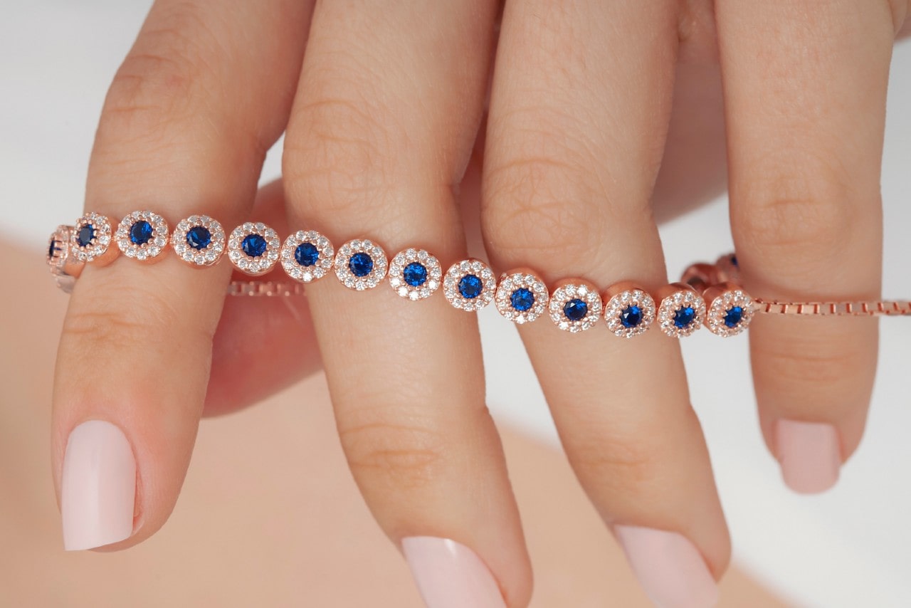 close up image of a woman’s hand holding a rose gold line bracelet featuring halo set sapphires