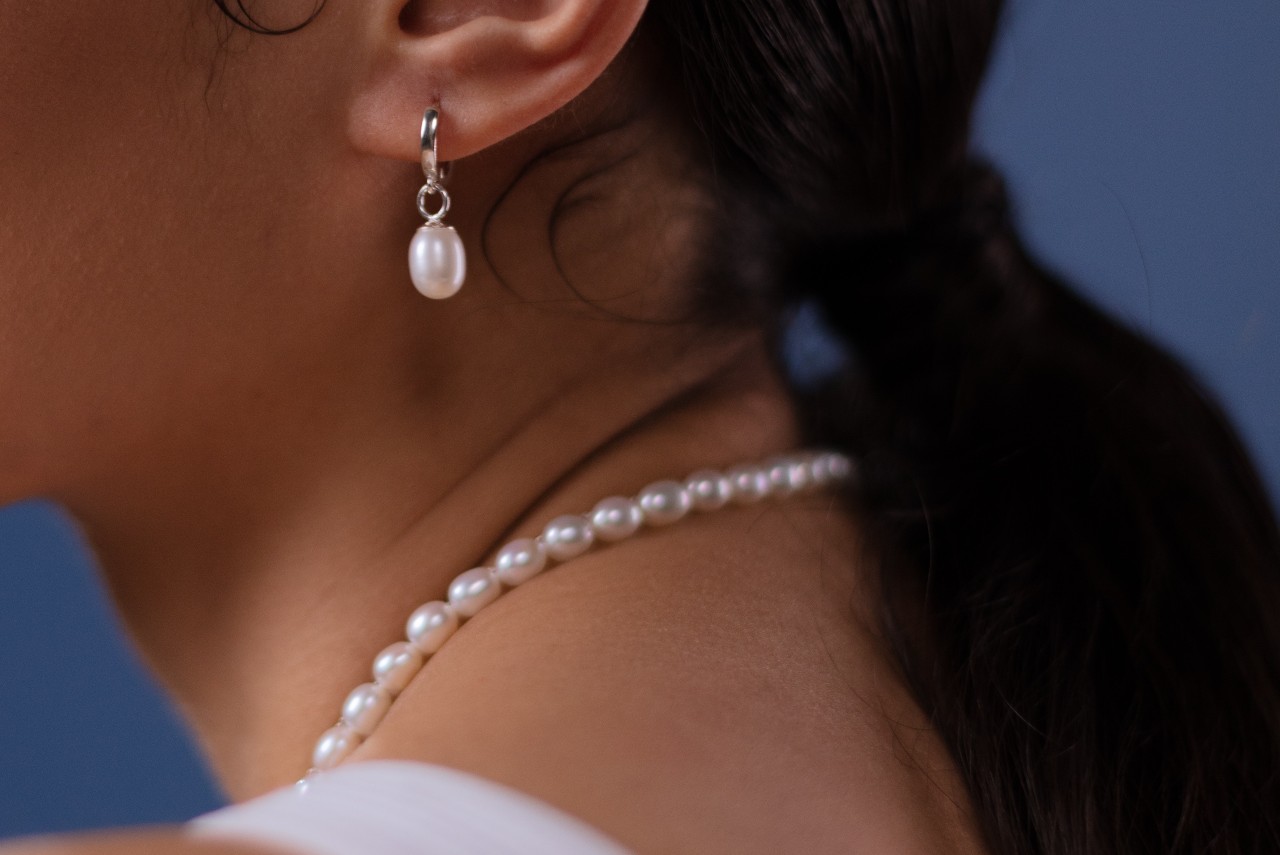 close up image of a woman wearing a pearl necklace and a pearl drop earring
