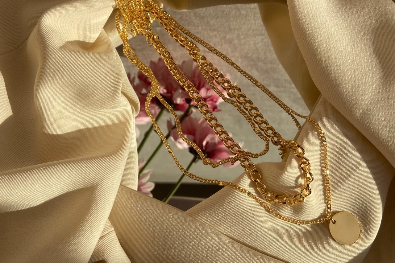 Three chain necklaces sit on a mirror, surrounded by beige fabric.