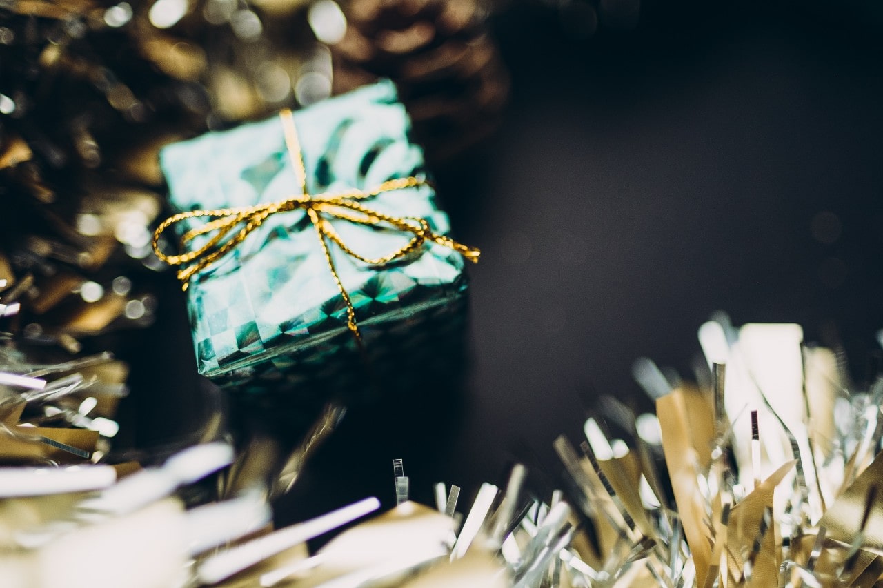 A small wrapped gift sits among gold tinsel on a black background.