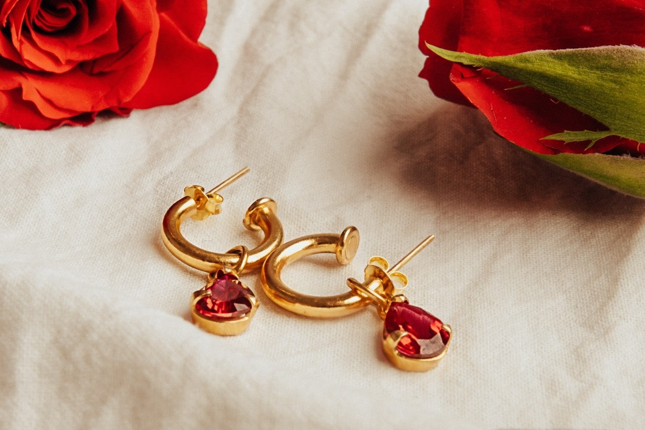 a pair of yellow gold huggie earrings with pear shape rubies lying on a piece of linen fabric