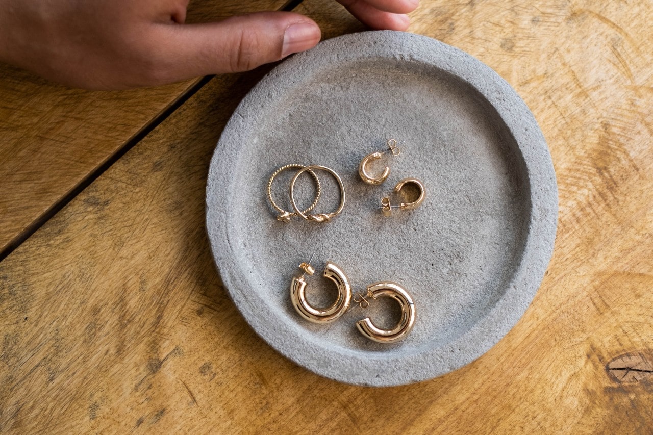 a cement dish holding three pairs of small, yellow gold huggie earrings
