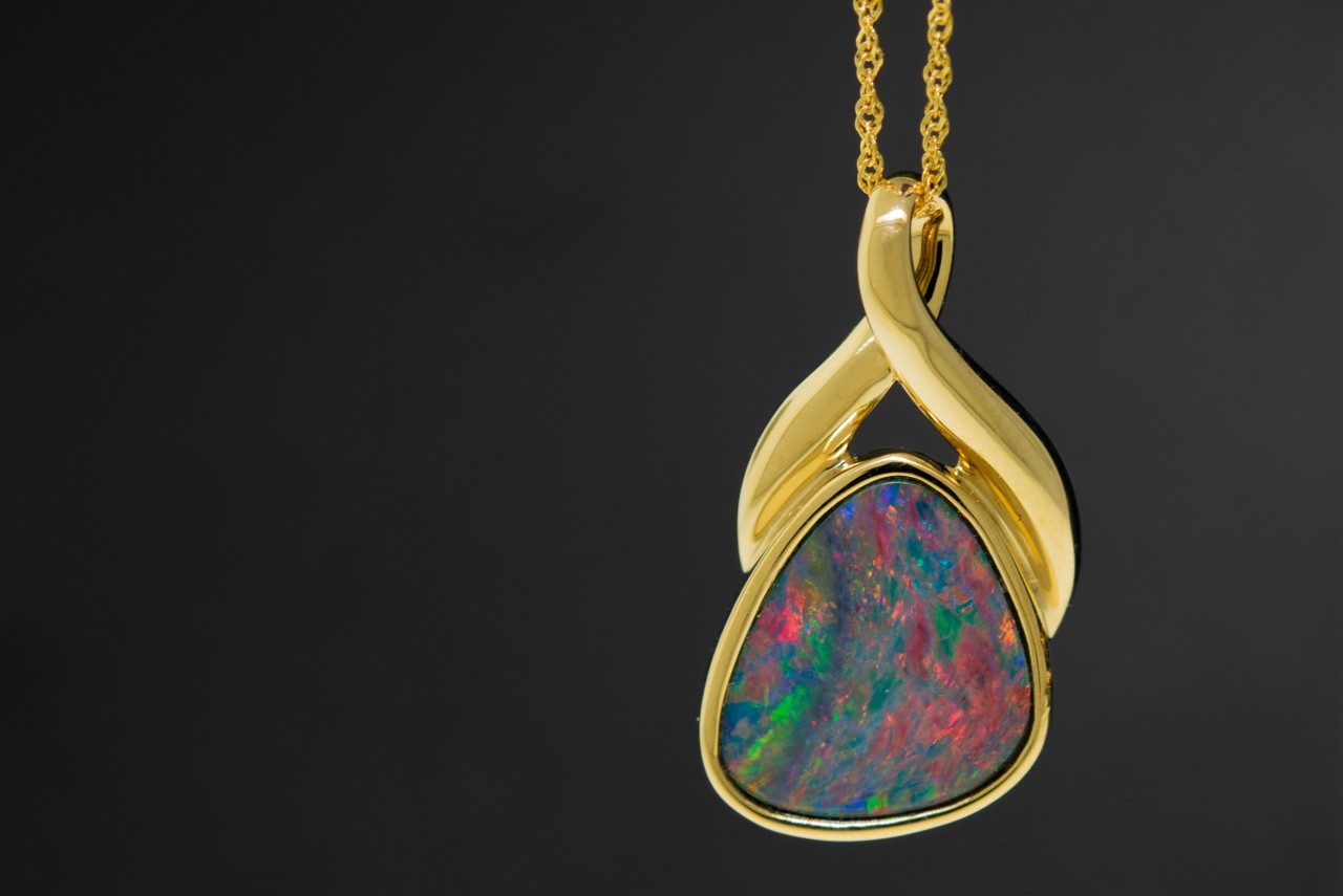 a yellow gold pendant necklace featuring an opal against a black background