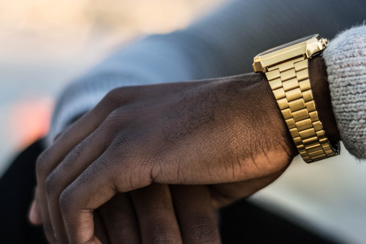 close-up image of a man’s hands, one wrist adorned with a luxurious yellow gold watch