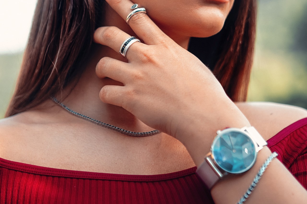 close-up image of a woman wearing a deep red blouse and a watch with a blue dial