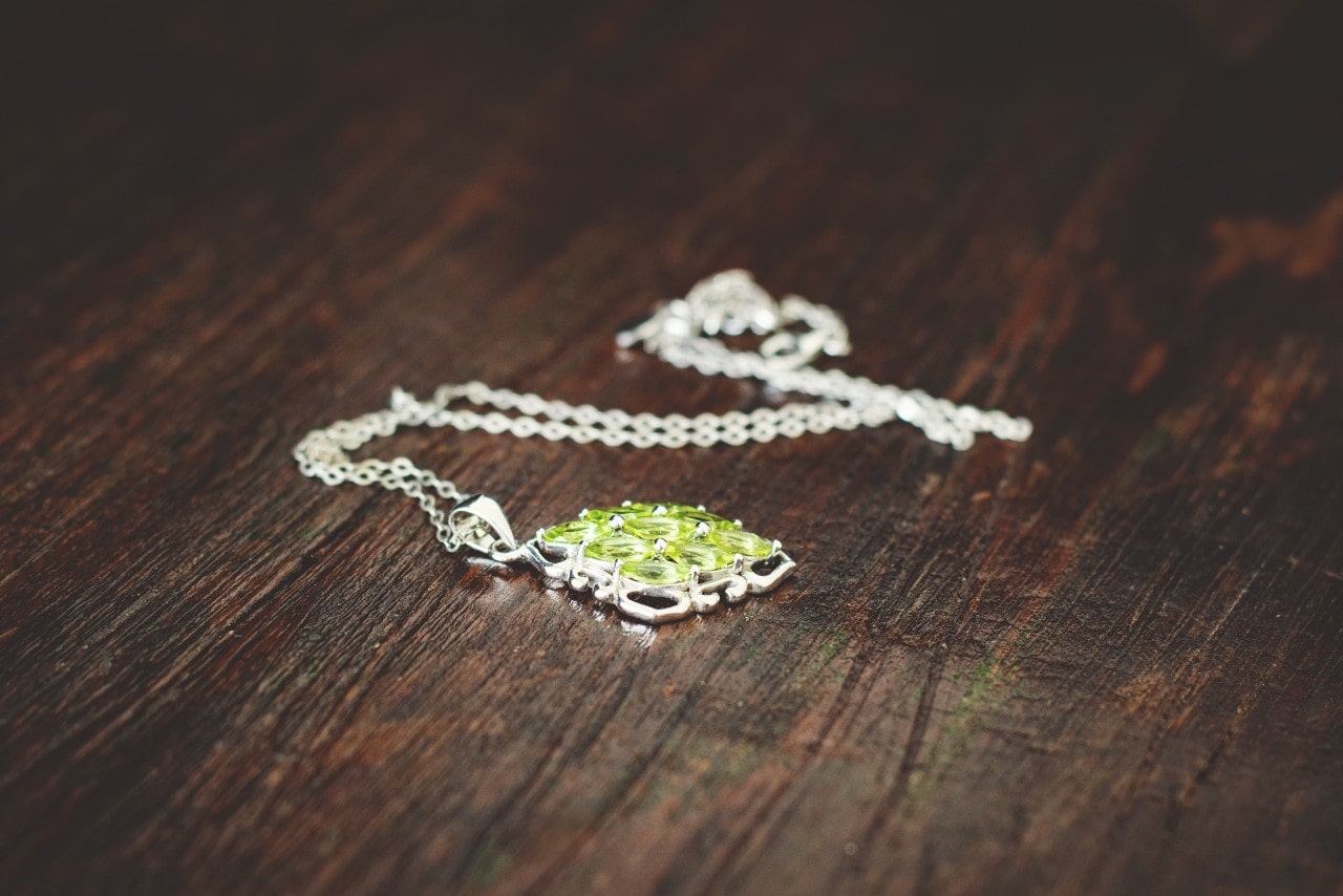 a platinum and peridot necklace on a wood surface