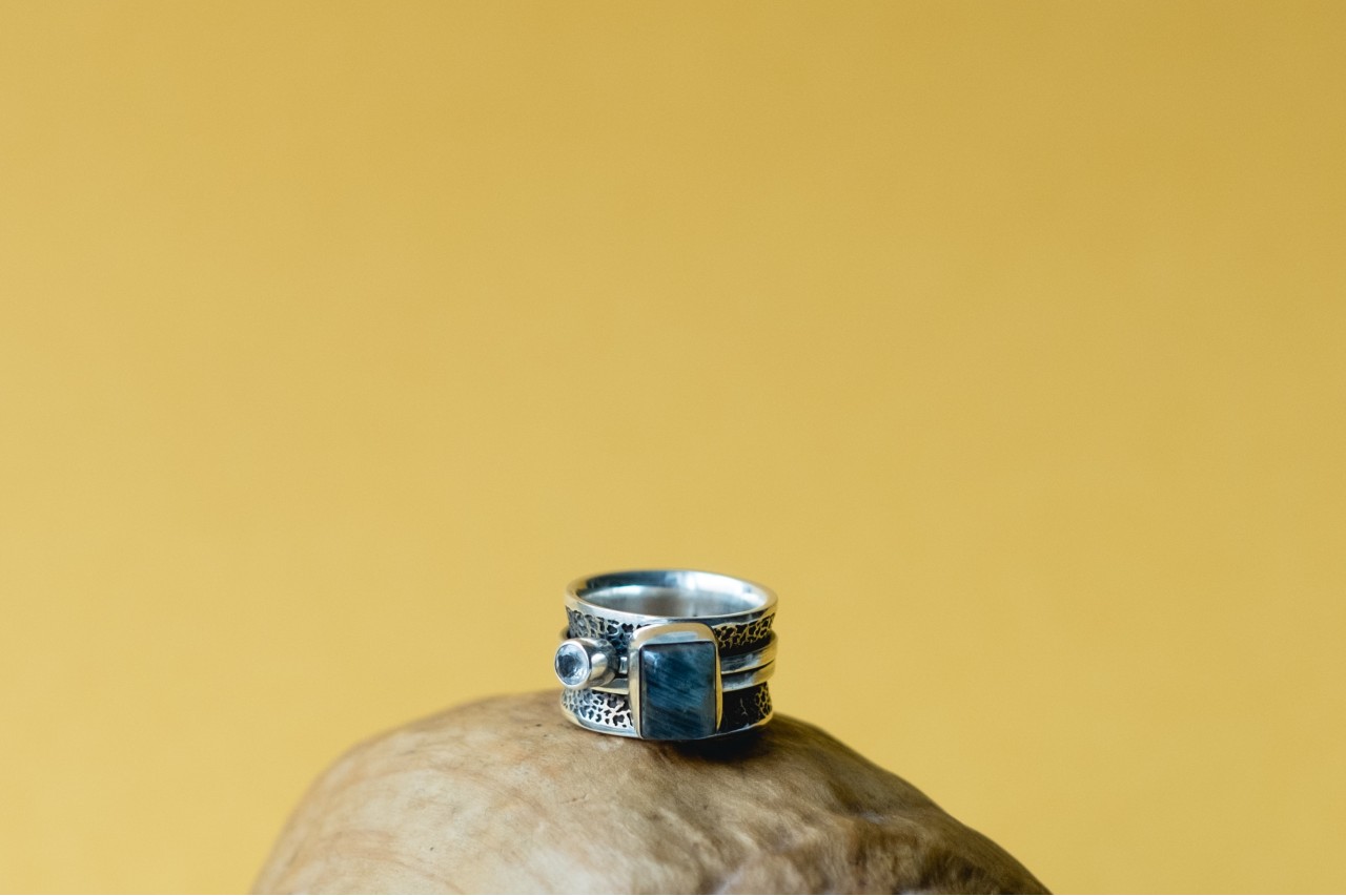 a silver fashion ring with a blue gemstone against a yellow background