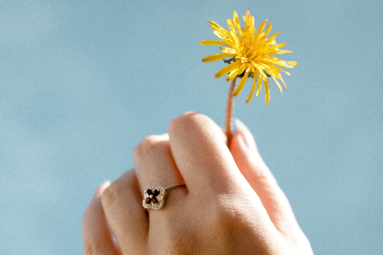 a hand holding a dandelion up to the sky and wearing a floral fashion ring