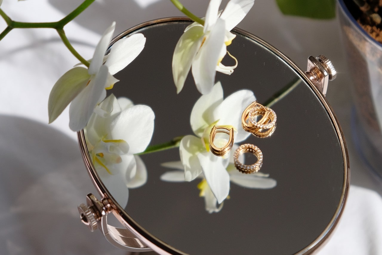 rings and earrings sitting on an upturned mirror next to flowers