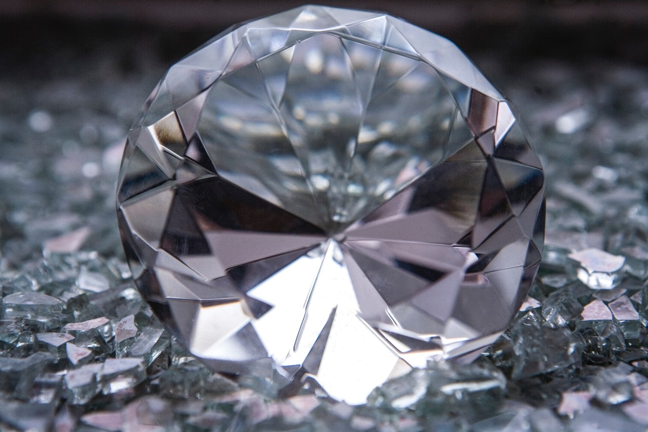 A round-cut diamond sits in a crowd of glass shards.