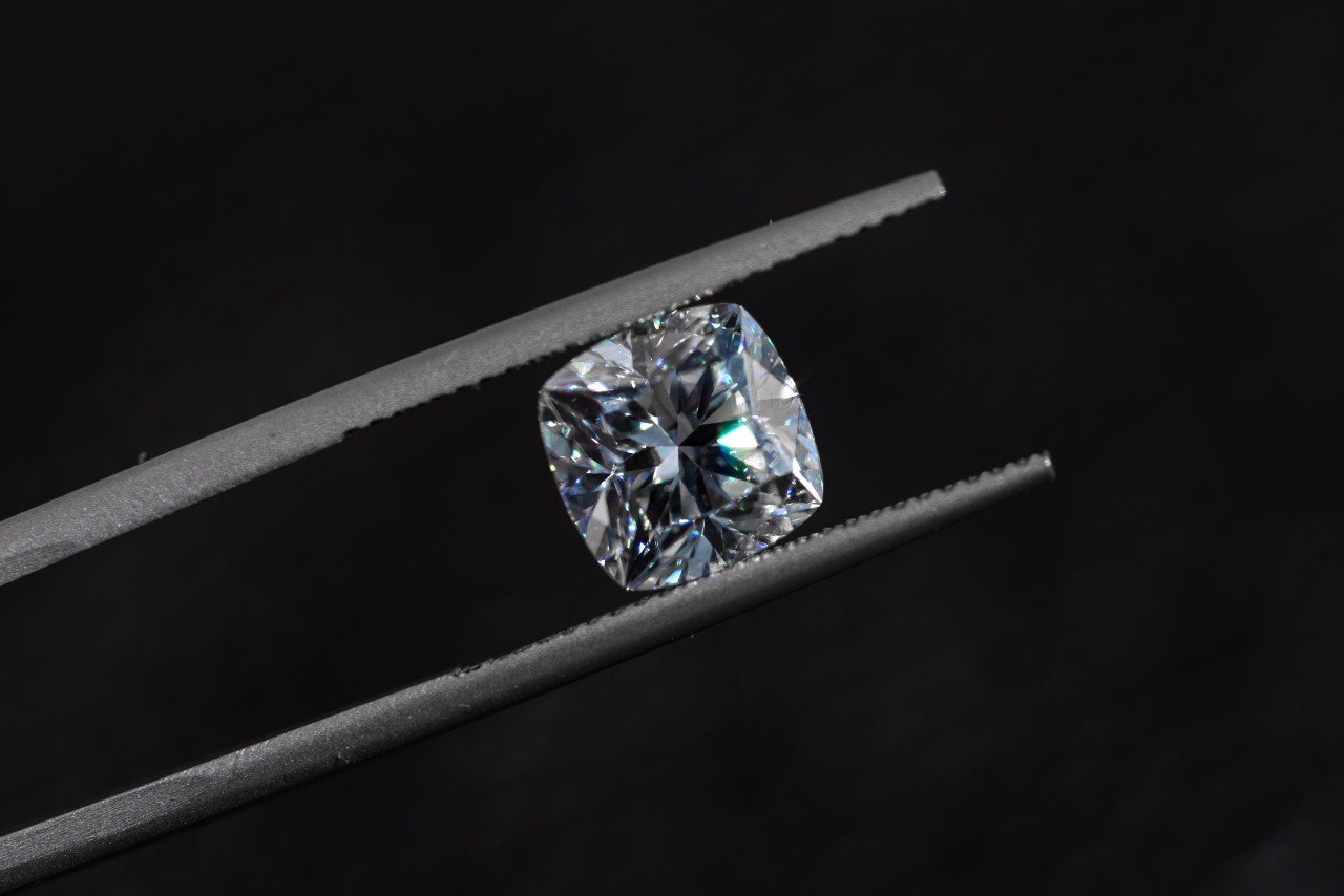 A cushion-cut diamond sits in a pair of tweezers.