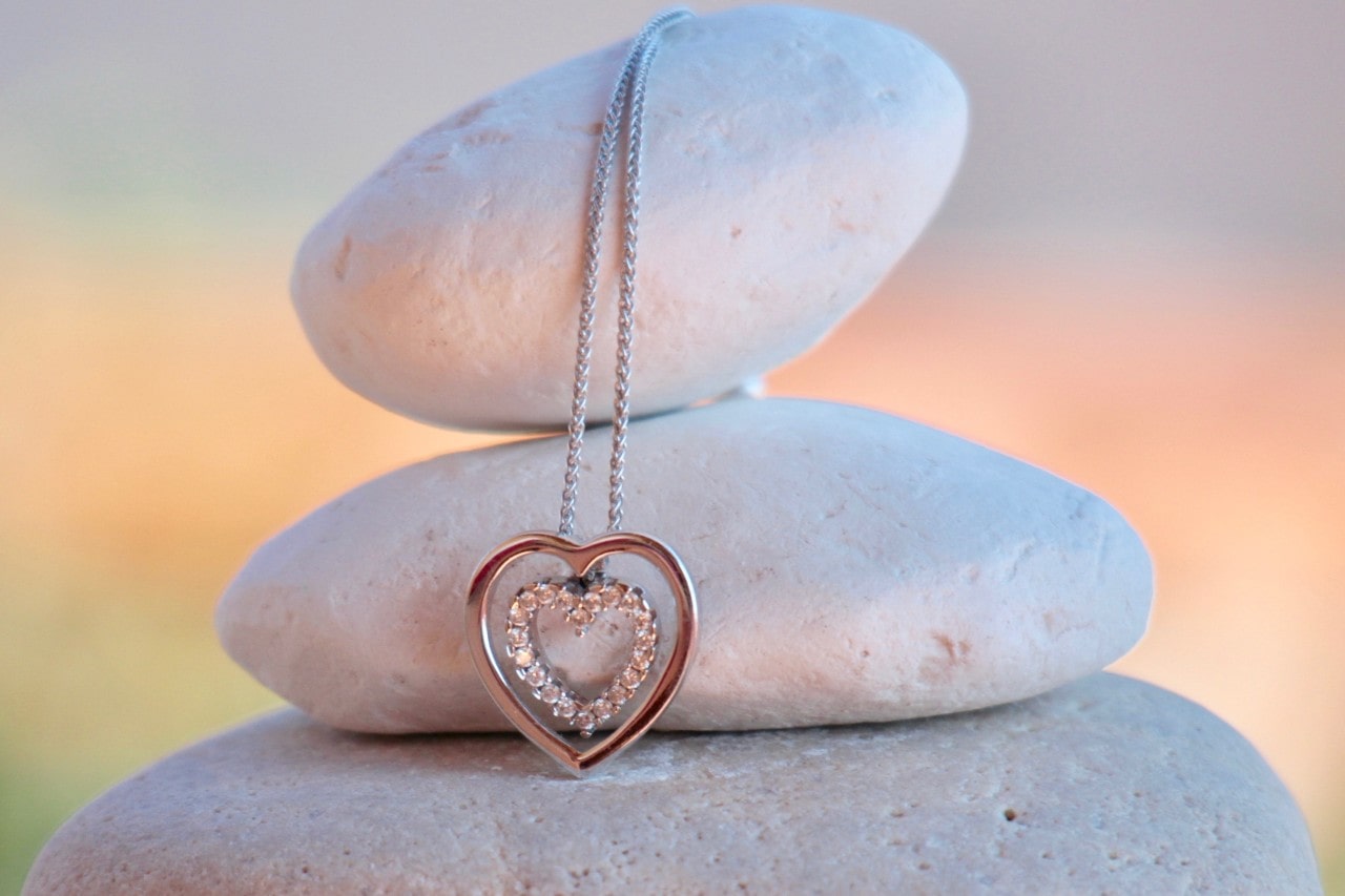 a heart-shaped diamond pendant hanging on a stack of rocks