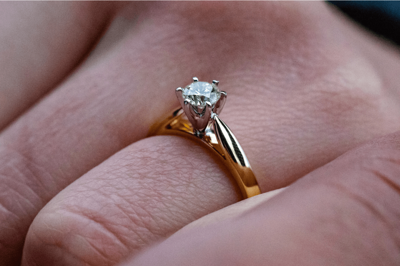A closeup of a yellow gold solitaire ring with a prong-set center diamond.