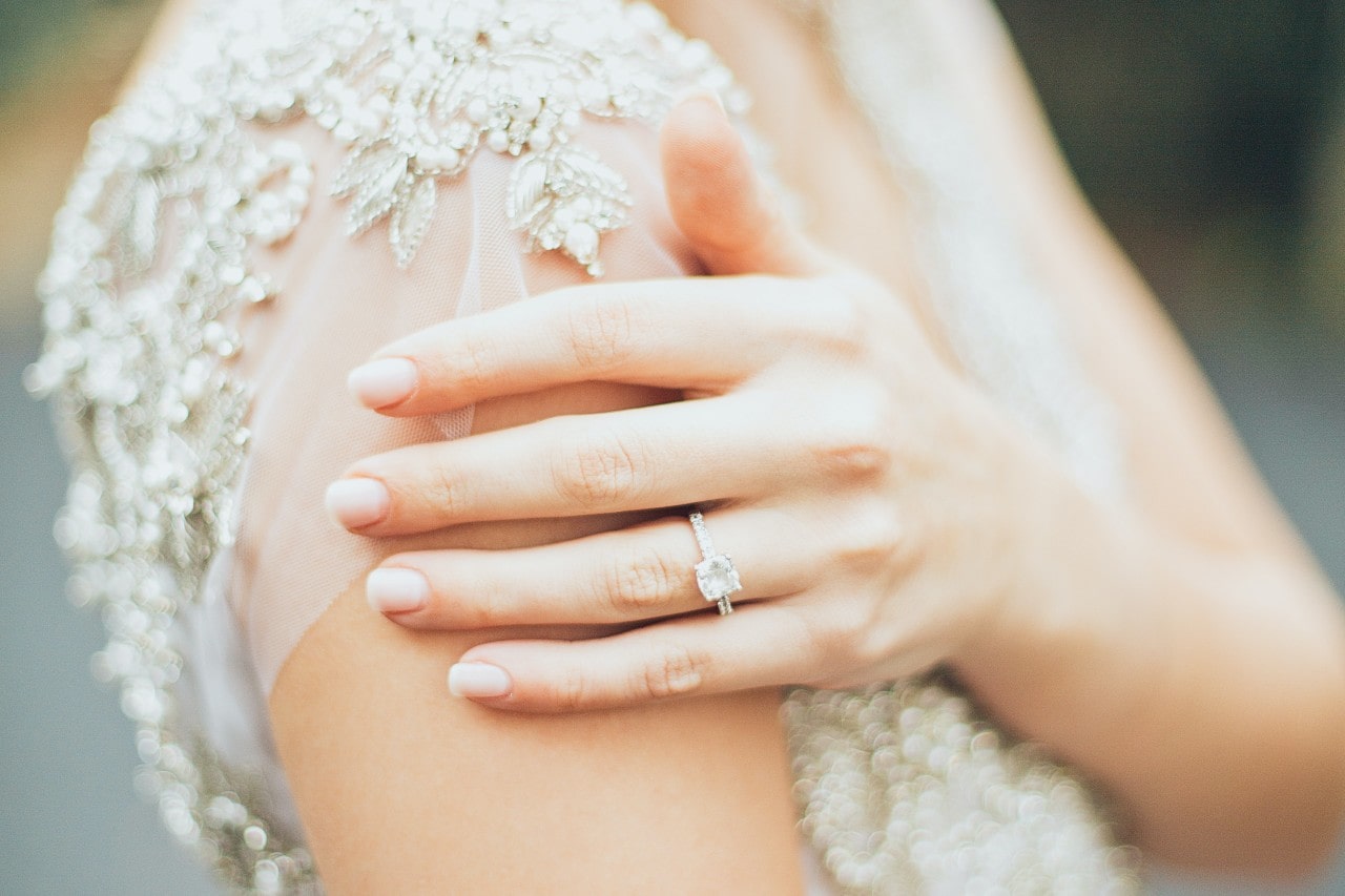 A bride brushes her shoulder, showing her princess-cut diamond engagement ring.
