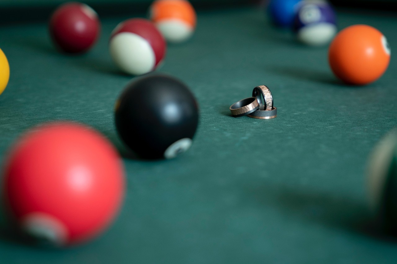 Three mixed metal men’s wedding bands sit together on a pool table.