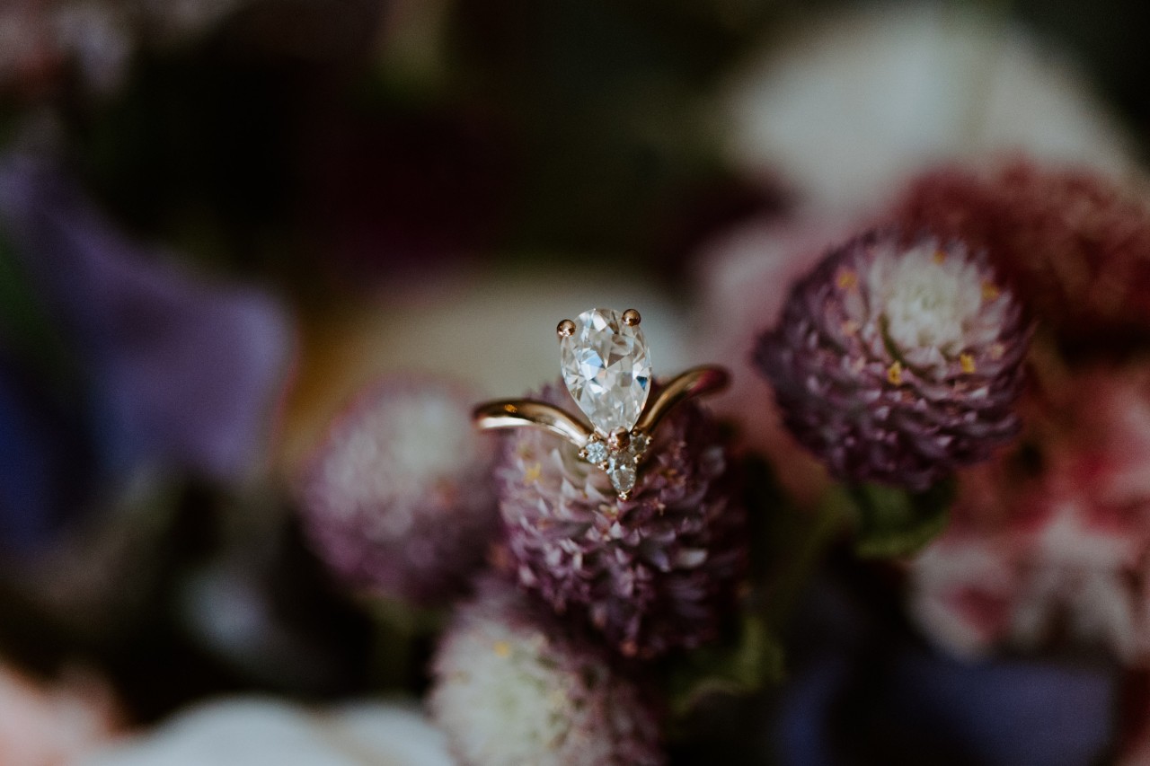A gold pear-shaped diamond engagement ring sits on a purple cone-shaped flower.
