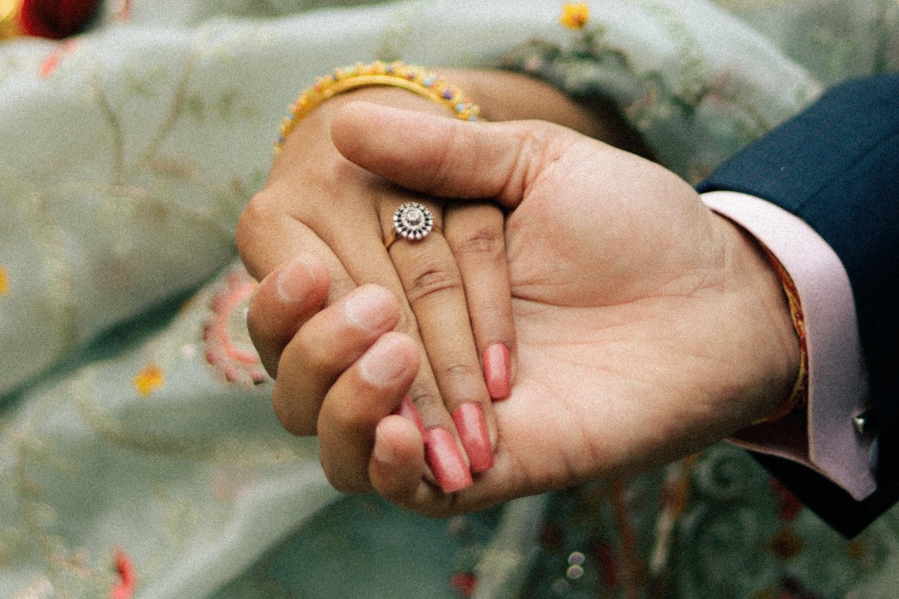 A couple holds hands, showing off a vintage halo round-cut ring.