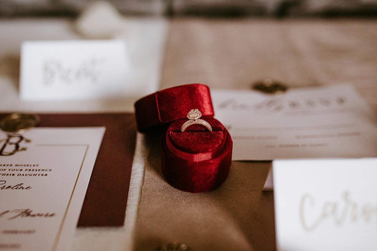 A round-cut ring in a red velvet ring box among wedding invitations.
