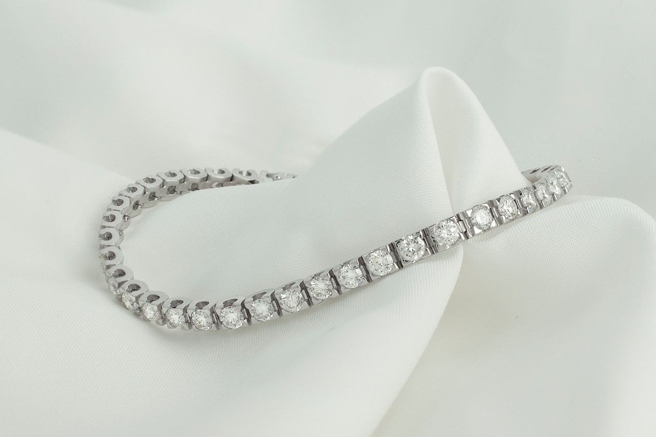 A silver, diamond tennis bracelet arranged on a white cloth