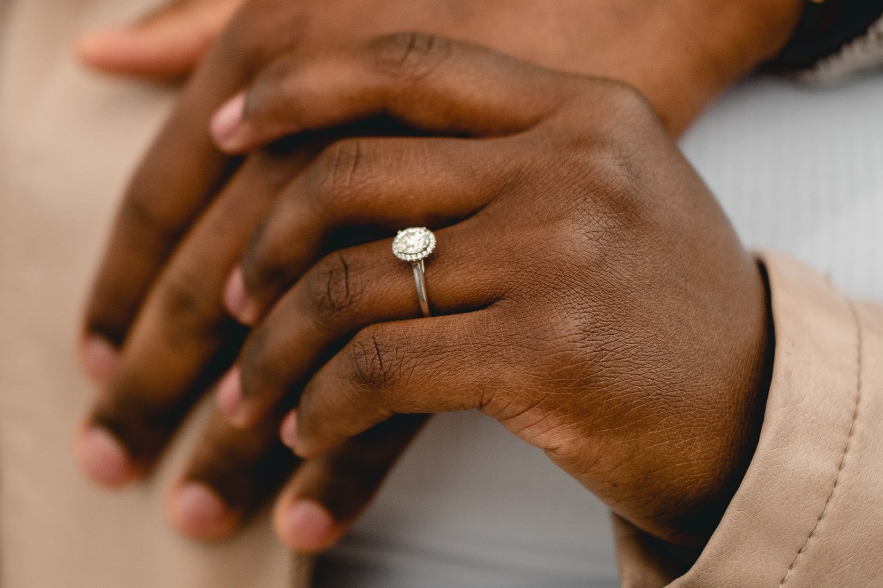 a woman’s hand holding a man’s hand, the woman’s donning a white gold engagement ring